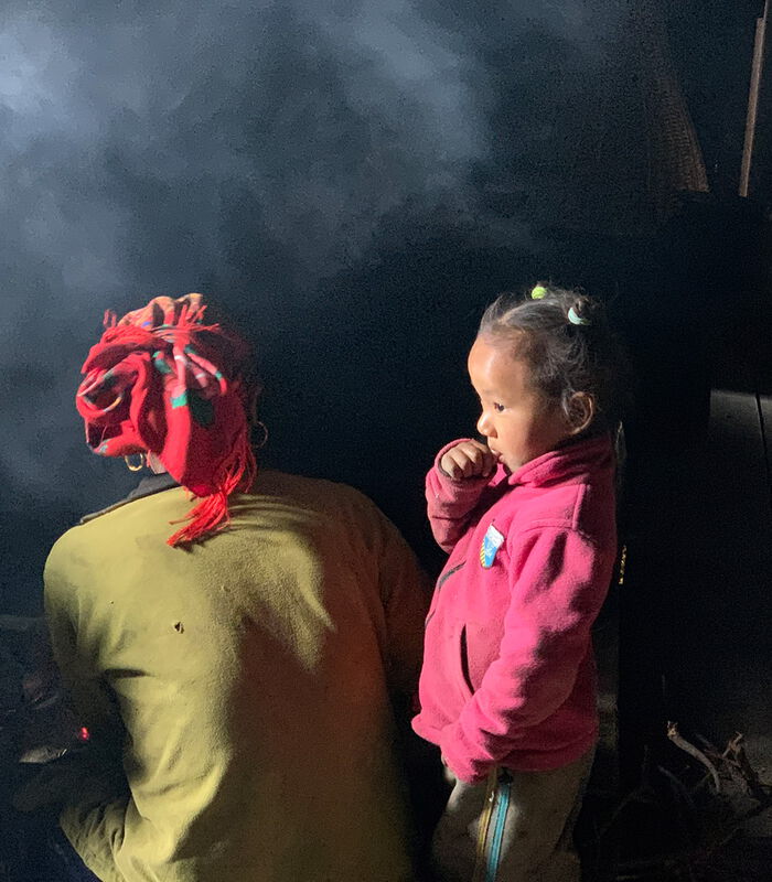 Eine nepalesiche Mutter mit Kind steht in einer recht dunklen Hütte am offenen Feuer im Ruach