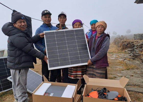 Einige Dorfbewohner halten gemeinsam ein neues Solarmodul. Auf dem Bild sind noch weitere technische Gerätschaften für die PV-Anlage zu sehen.