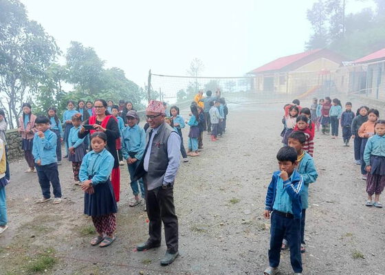 Nepalesiche Kinder und Erwachsene stehen zusammen auf einem Sportplatz. Im Hitnergrund sind Häuser zu sehen.