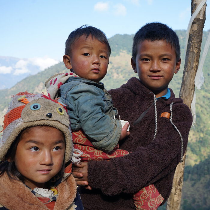 Ein neplesiches Mädchen und ein Junge mit einem kleinen Kind auf dem Arm vor einem Berg im Himalaya.