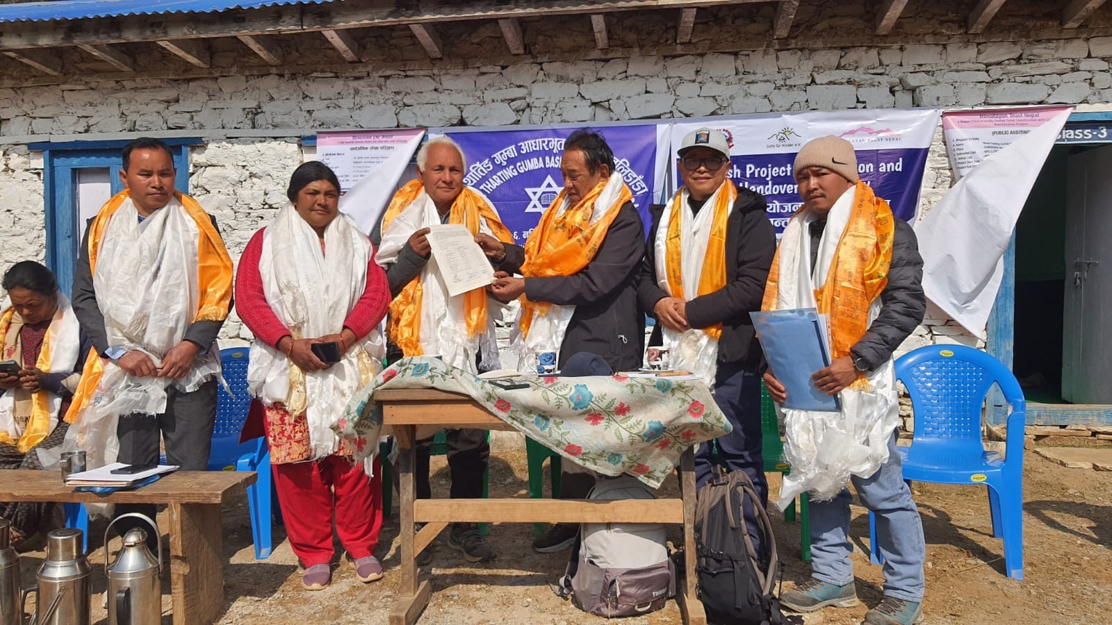 Fünf Personen in feierlicher Kleidung tauschen Dokumente vor einem Gebäude aus.